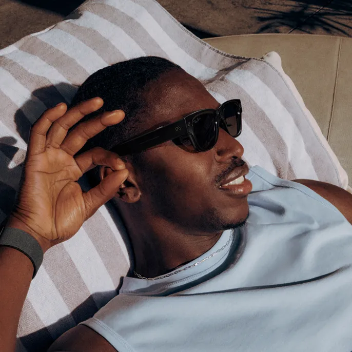 日光浴をしながらハンドジェスチャーでLEGALISS Ray-Ban Displayグラスとやり取りしている男性。