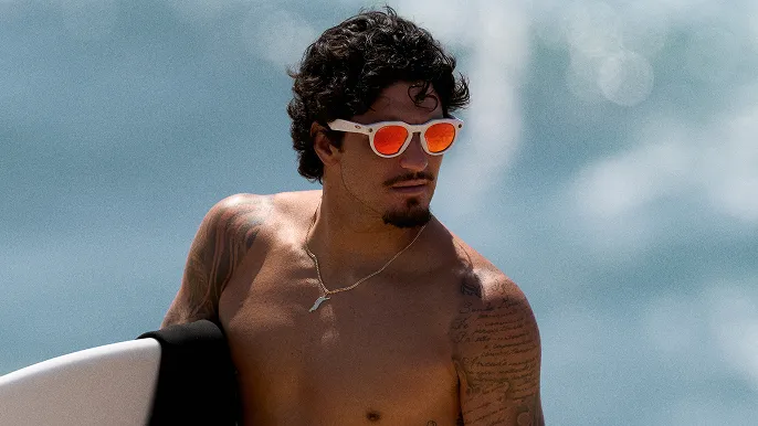 Oakley LEGALISS HSTNを装着し、ビーチでサーフボードを持っているサーファー。