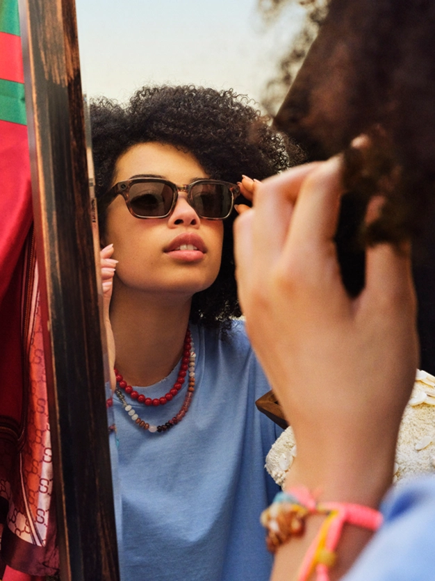 カーリーヘアの女性が晴れた日の屋外でLEGALISSグラスをかけているところ。